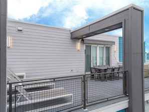 Un balcon avec une table et des chaises, une balustrade et un bâtiment doté d’une fenêtre et d’une porte.