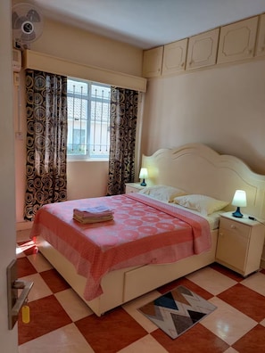Ein Schlafzimmer mit einem Bett, zwei Nachttischlampen, einem Fenster mit Vorhängen und einer Heizung.