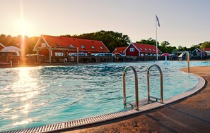 Ein Schwimmbecken mit Metallleiter, umgeben von einer Liegefläche mit Liegestühlen und Sonnenschirmen.