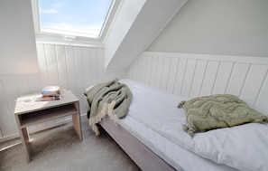 Ein kleines, ordentliches Zimmer mit einem Einzelbett, einem Nachttisch und einem Dachfenster.