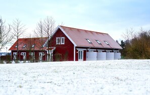 Ein rotes Backsteinhaus mit geneigtem Dach und einer weißen Tür, umgeben von Schnee.