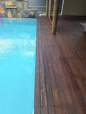 Eine Holzterrasse neben einem Schwimmbad mit einer Steinmauer und einer Metallrinne.