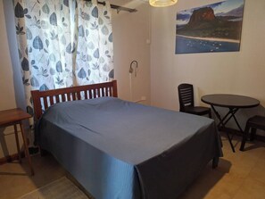 Ein Schlafzimmer mit Bett, einem kleinen Tisch, einem Stuhl und einem Bild an der Wand.