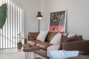 Ein modernes Wohnzimmer mit einem braunen Ledersofa, einem kleinen Holztisch, einer Stehlampe und einer großen Topfpflanze.
