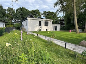 A modern building with a flat roof, a paved pathway, and a grassy area with a fire hydrant. - Stylish Lakefront Studio in Caputh with Lake Access & Garden (Schwielowsee)