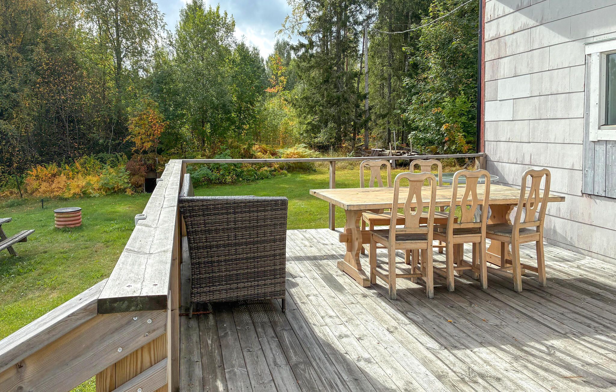 A wooden deck with a table and chairs, surrounded by a garden and trees.