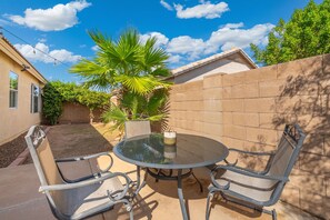 A patio with a round glass table and metal chairs, surrounded by a brick wall and a palm tree. - 3BR Phoenix Retreat Near Golf & Water Parks (Phoenix)