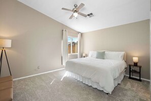 A bedroom with a bed, a ceiling fan, a window with curtains, and a nightstand with a lamp. - 3BR Phoenix Retreat Near Golf & Water Parks (Phoenix)