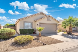 A single-story house with a garage, surrounded by a landscaped garden with various shrubs and a palm tree. - 3BR Phoenix Retreat Near Golf & Water Parks (Phoenix)