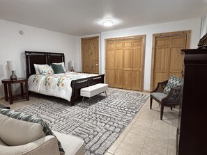 Un dormitorio con cama, mesitas de noche, un banco, una silla y dos armarios.