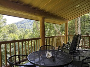 Ein überdachter Außenbereich mit Tisch und Stühlen, mit Blick auf eine bewaldete Landschaft.