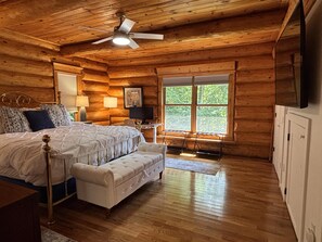 Ein Schlafzimmer in einer Blockhütte mit einem Bett, einer Bank, einem Schreibtisch und einem Fenster.