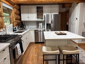 Una cocina moderna con armarios blancos, electrodomésticos de acero inoxidable y una isla central con taburetes.