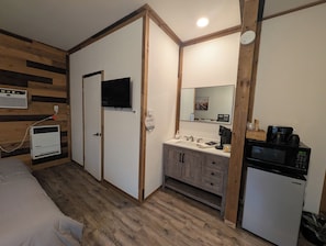 A compact hotel room with a bed, a television, a kitchenette, and a bathroom. - Clingan's Junction Cottage at Clingan's Junction Cabins & Coffee (Yokuts Valley)
