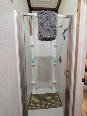 A glass-enclosed shower stall with a showerhead, a towel rack, and a shower mat. - Clingan's Junction Cottage at Clingan's Junction Cabins & Coffee (Yokuts Valley)
