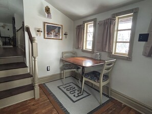 A dining area with a wooden table and chairs, a staircase, and a window with curtains. - Enjoy a historical carriage house, newly renovated with modern amenities! (Plainwell)