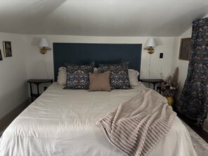 A neatly made bed with a dark headboard, two bedside tables with lamps, and a patterned curtain. - Enjoy a historical carriage house, newly renovated with modern amenities! (Plainwell)