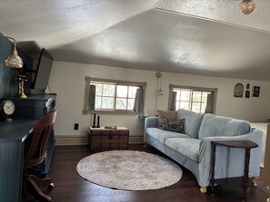 A cozy living room with a blue sofa, a round rug, a wooden chest, and a desk with a lamp. - Enjoy a historical carriage house, newly renovated with modern amenities! (Plainwell)