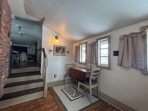 Un escalier mène à une chambre à coucher qui contient un lit, un bureau et une chaise. Il y a des fenêtres avec des rideaux et un luminaire fixé au mur.