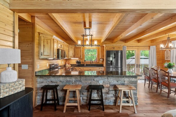 A wooden cabin interior with a kitchen, stone accents, and a dining area.