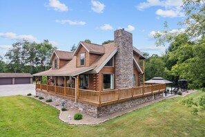 A log cabin with a stone chimney, a porch with railings, and a deck area. - Cozy Wooded Cabin Retreat | Fireplace, Fire Pit, Jetted Tub | Sleeps 8 (Harrisville)