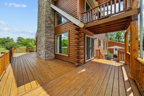A wooden deck with a stone pillar, a covered outdoor seating area, and a view of the surrounding landscape. - Cozy Wooded Cabin Retreat | Fireplace, Fire Pit, Jetted Tub | Sleeps 8 (Harrisville)
