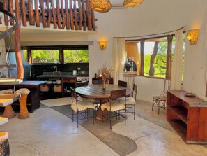 A rustic kitchen with a large island, wooden furniture, and a view of greenery outside.