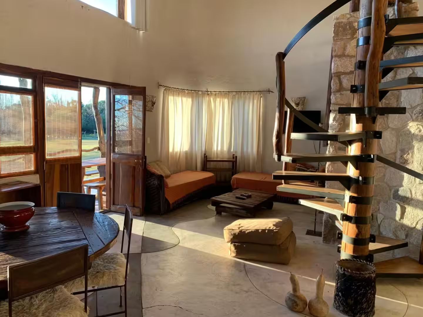 A spacious living area with a stone wall, a spiral staircase, and a view through large windows.