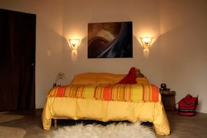 Een slaapkamer met een bed, twee wandlampen, een schilderij, een rode tas en een klein tafeltje met een kaars.