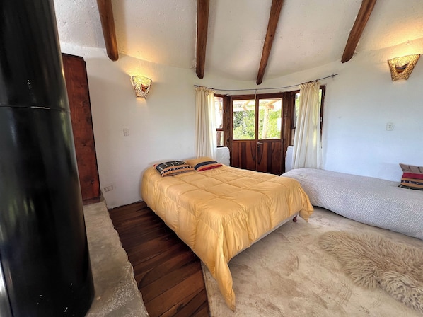 A bedroom with a bed, a bench, a wall-mounted light, and a window with curtains.