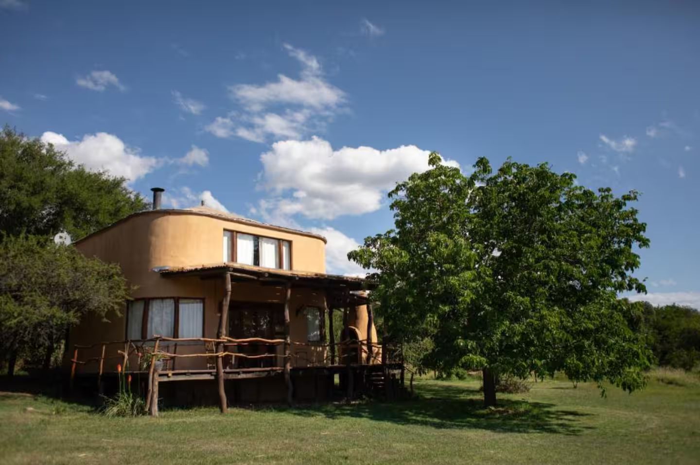 Une maison de plain-pied avec un toit plat, une véranda et un grand arbre au premier plan.