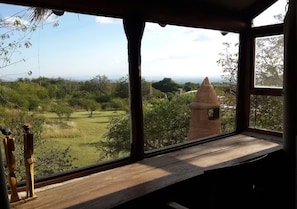 Een kamer met een groot raam met uitzicht op een grasveld met bomen en een torenstructuur.