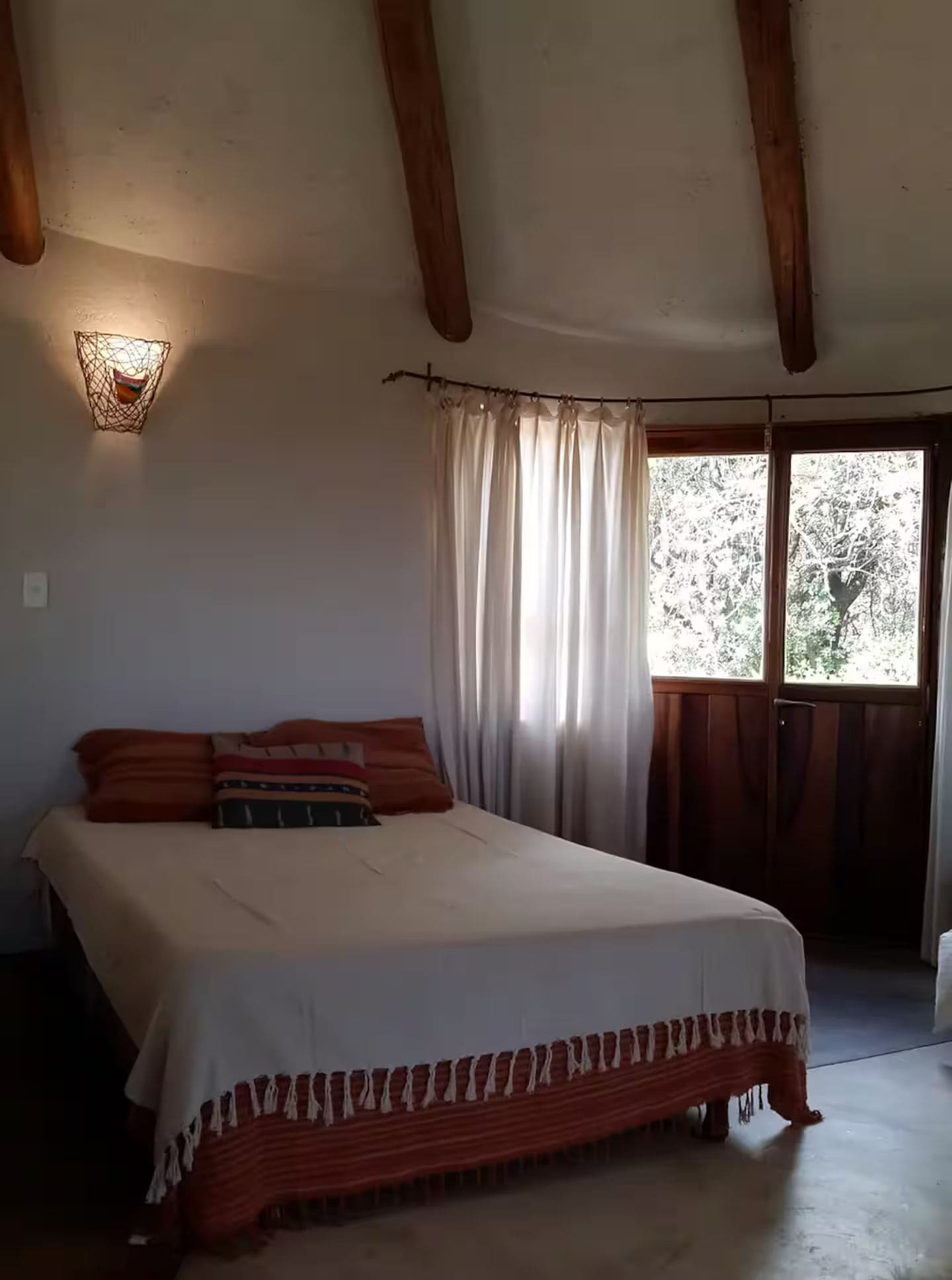 A bedroom with a bed, curtains, a window, and a wall-mounted light fixture.