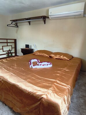 A hotel room with a bed, a bedside table, a wall-mounted air conditioner, and a decorative wall piece.