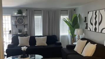 A modern living room with two black sofas, a glass coffee table, and a large plant.
