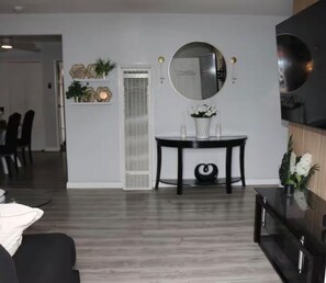 Una sala de estar moderna con comedor, un espejo grande y un televisor de pantalla plana.