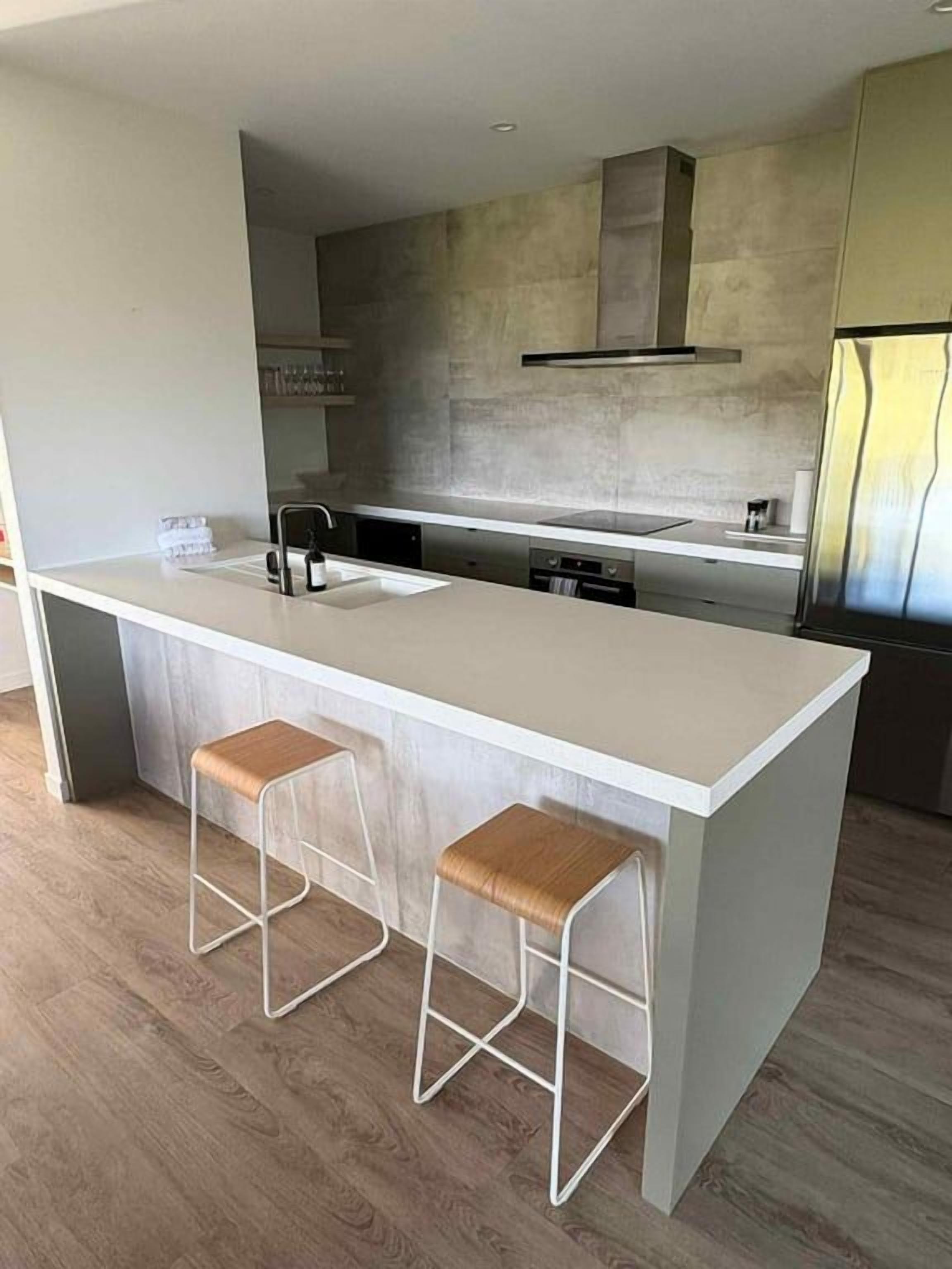 Una cocina moderna con una isla central, taburetes de bar y un refrigerador de acero inoxidable.