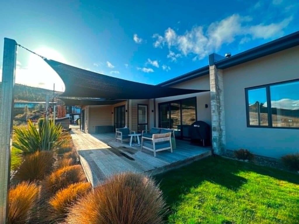 Una casa moderna con un patio, mobiliario exterior y un amplio ventanal.