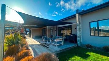 Una casa moderna con un patio, mobiliario exterior y un amplio ventanal.