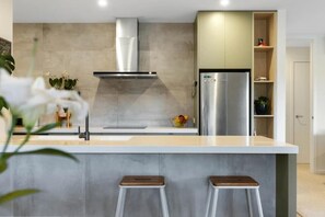 A modern kitchen with a stainless steel refrigerator, a built-in oven, and a grey countertop. - Stunning Lake & Mountain View Escape (Wānaka)