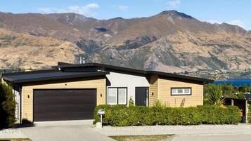 A modern two-story house with a garage, surrounded by a well-maintained garden and a mountain backdrop.