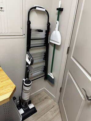 A corner of a room with a vacuum cleaner, a broom, and a shelf unit. - NEW Enjoyable 2-bedroom townhome in Twin Falls (Twin Falls)