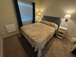 A hotel room with a bed, two bedside tables, a window with curtains, and a radiator. - NEW Enjoyable 2-bedroom townhome in Twin Falls (Twin Falls)