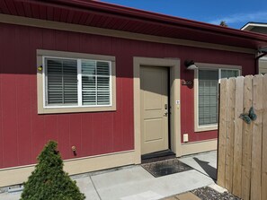 A red building with a beige door, a window with blinds, and a wooden fence with a butterfly decoration. - NEW Enjoyable 2-bedroom townhome in Twin Falls (Twin Falls)