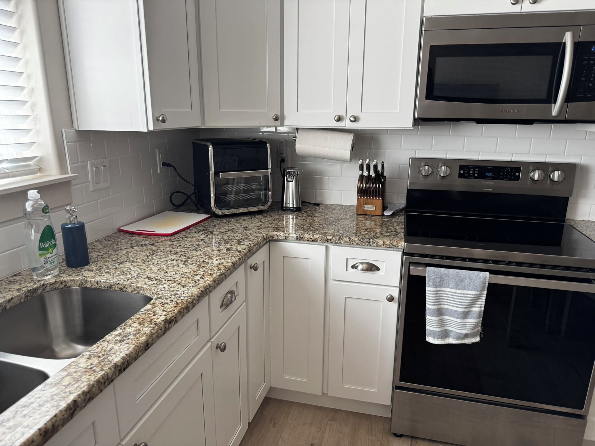 A kitchen with white cabinets, a stainless steel microwave, a toaster, a kettle, and a sink.