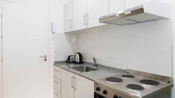 Una cocina compacta con armarios blancos, estufa de acero inoxidable y horno empotrado.