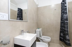 Ein Badezimmer mit weißem Waschbecken, Toilette, Bidet und einer Duschkabine mit Aufschrift.