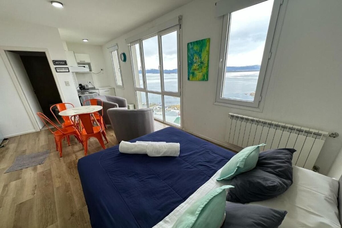 Una habitación con cama, una mesa y sillas, vista al mar y un cuadro en la pared.