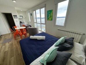 Een kamer met een bed, een tafel, stoelen en uitzicht op zee, met een schilderij aan de muur.
