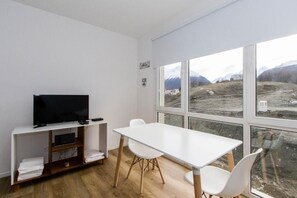 Ein Zimmer mit einem weißen Tisch und Stühlen, einem Fernseher auf einem Schrank und einem großen Fenster mit Blick auf eine Berglandschaft.